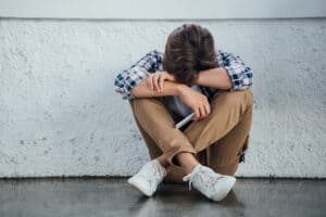 sad teenager sitting with crossed legs and holding smartphone